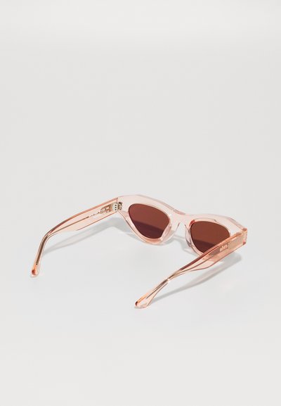 Ochelari de soare cu nuanțe roz, cu rame transparente, în formă de pisică, și lentile de culoare maro închis. Au brațe subțiri, curbate, cu detalii subtile de branding.