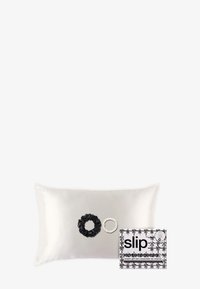Cojín de seda en color crema claro con cintas para el cabello en blanco y negro en la parte frontal. Acompañado de un juego de regalo en caja con acentos florales.