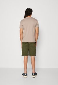 Beige kortærmet t-shirt parret med olivenfarvede shorts, der har lommer og en lille patchdetalje, set fra ryggen.