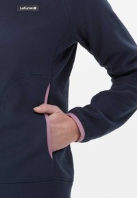Chaqueta de forro polar navy con un ribete rosa en los puños y los bolsillos, con un diseño ajustado y un parche con el logo en el pecho.