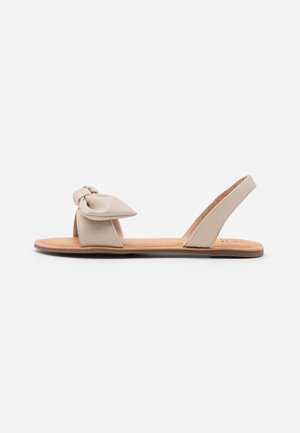 Beige leren sandaal met een geknoopt detail op het bovenwerk, voorzien van een platte zool en een slingback-ontwerp. Gladde textuur en minimalistische stijl.