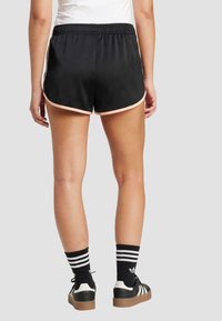 Svarta sportshorts med elastisk midja, med en ljusrosa kant längs fållen. Matchas med svartvita randiga strumpor och sneakers.