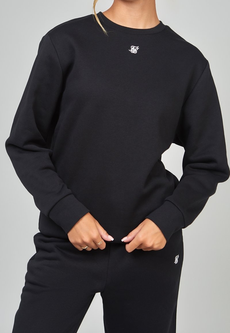 Sudadera negra hecha de algodón suave, con mangas largas, un cuello redondo y un pequeño logotipo blanco en el pecho.