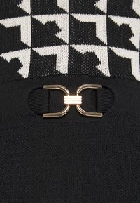 Tissu tricoté à motif pied-de-poule noir et blanc sur un tricot uni noir avec un petit détail de boucle métallique dorée centré sur la couture.