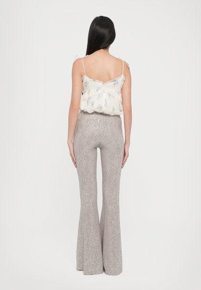 Top leggero color crema con stampa floreale e spalline regolabili, abbinato a pantaloni grigi a zampa d'elefante aderenti con un design lucido e di texture.