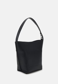 Sac seau en cuir noir avec une large bandoulière et un détail de poche subtilement cousu sur le côté.