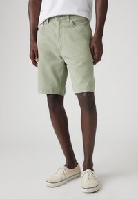 Khaki zelené denimové šortky so striženým strihom, dizajnom s piatimi vreckami a pútkami na opasok. Nosené s off-white teniskami.