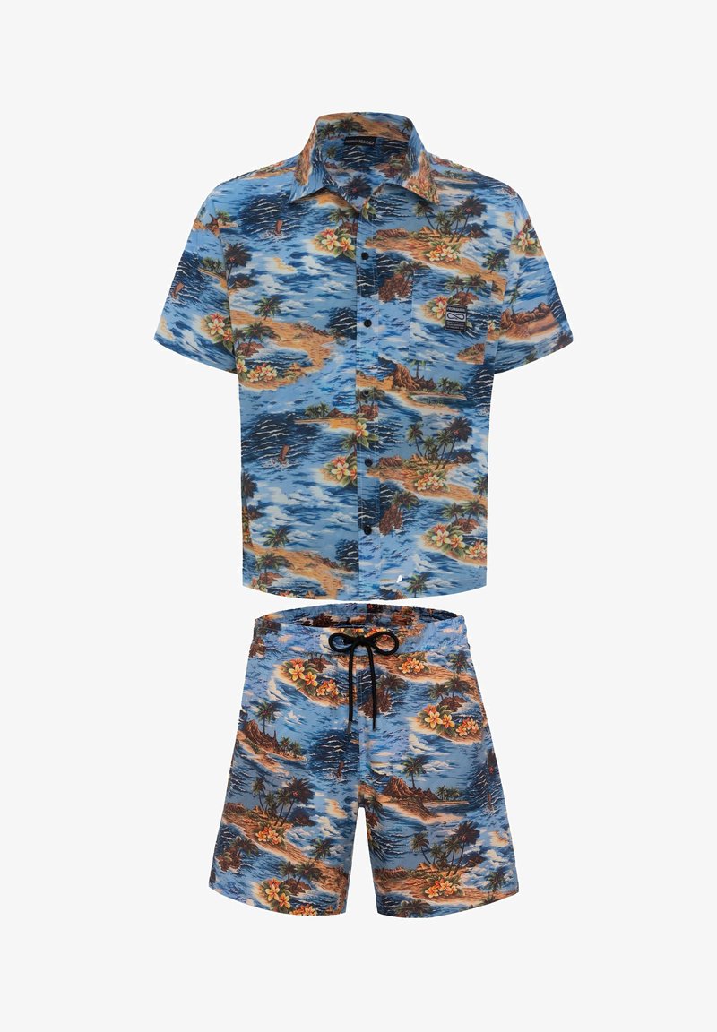 Camicia a maniche corte con bottoni e pantaloni corti coordinati, entrambi con una stampa tropicale blu che presenta isole, palme e fiori in colori vivaci.