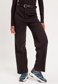 Pantaloni neri a gamba larga con vita alta, dotati di una cintura con fibbia argentata. Abbinati a sneakers sportive multicolori.
