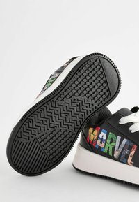 Baskets noires ornées de graphismes de personnages Marvel sur les côtés, avec des lacets blancs et des semelles en caoutchouc noir texturé avec des motifs en zigzag.