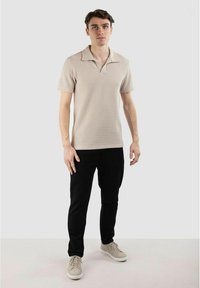 Beige randig polo t-shirt med kortärmar och krage, i kombination med svarta byxor och ljusa sneakers. Enkelt, figursytt design.