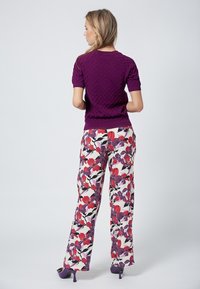 Suéter morado de manga corta y textura con un patrón de diamantes, combinado con pantalones de pierna ancha con un diseño floral en rojo, morado y negro.