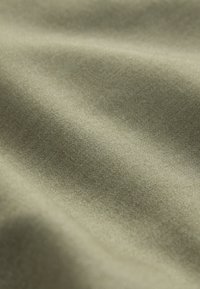 Kokvilnas audums maigi olīvzaļā krāsā ar gludu, mīkstu tekstūru, smalku spīdumu un smalku pinumu, krītoties maigos viļņos.