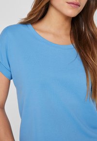 T-shirt bleu clair avec un col rond et des manches courtes. Texture de tissu lisse, présentant un design simple sans motifs ni accents visibles.