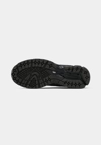 Semelle de chaussure de sport noire présentant un motif de grip texturé avec des formes hexagonales et circulaires, conçu pour la traction et la stabilité.