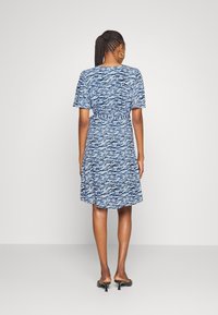 Blå mönstrad klänning med korta ärmar, insvängd midja och utsvängd kjol. Har en vågig design, tillverkad av lätt tyg och matchad med svarta klackar.