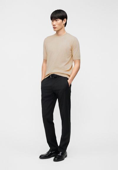 Μπεζ πουλόβερ με κοντά μανίκια από μαλακό υλικό, σε συνδυασμό με μαύρο, ραμμένο παντελόνι και μαύρα παπούτσια. Απλός σχεδιασμός, χωρίς σχέδια ή λογότυπα.