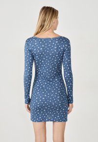 Abito attillato a maniche lunghe in denim blu, con un motivo floreale bianco. Tessuto morbido, scollo rotondo e lunghezza a metà coscia.