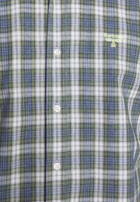 Chemise boutonnée à motif à carreaux bleu, vert et blanc avec petit logo Barbour jaune sur la poitrine.