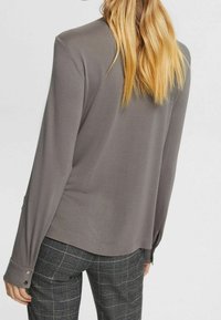 Haut gris à manches longues avec une coupe décontractée, présentant des poignets boutonnés et une texture lisse. Assorti à un pantalon à motif tartan.