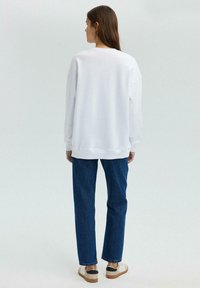 Witte oversized sweatshirt met verlaagde schouders, gecombineerd met blauwe rechttoe-rechtaan jeans en beige sneakers. Minimalistisch ontwerp met strakke lijnen.