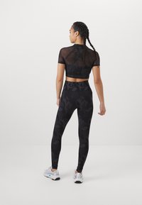 Zwart sportoutfit bestaande uit een cropped mesh top en hoge taille leggings met een tonale camouflageprint. Schoeisel omvat witte trainers.