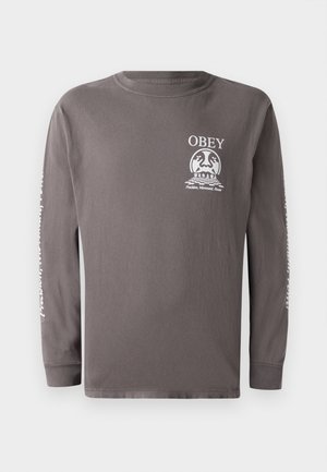 Camiseta de algodón gris de manga larga con cuello redondo. En el frente presenta el logo y gráfico "OBEY"; la manga derecha tiene un acento de texto en blanco.