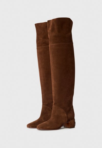 Botas de ante marrón hasta el muslo con punta afilada, tacón grueso y diseño sin costuras, que presentan una costura sutil y una textura suave.