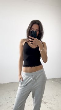 Camisola preta com rendas e calças de sweat cinza claro. A camisola apresenta alças finas, um design justo e uma bainha em forma de onda. Look casual.