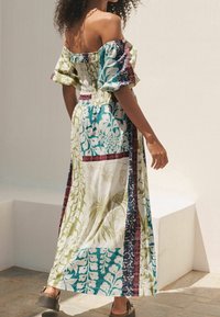 Robe maxi à épaules dénudées, à motif floral avec un buste froncé, présentant des accents verts, bleus et bordeaux, en tissu de coton léger.