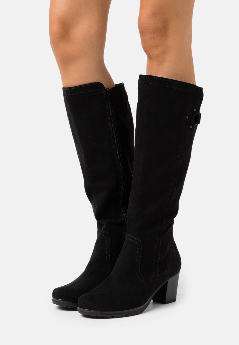 Bottes hautes en daim noir jusqu'au genou avec fermeture éclair latérale et talon bloc, portées sur des jambes nues sur fond blanc.