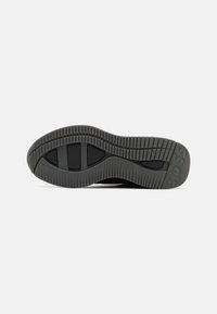 Semelle d'une chaussure noire avec des motifs imprimés et le mot "BOSS" embossé près du talon sur fond blanc.
