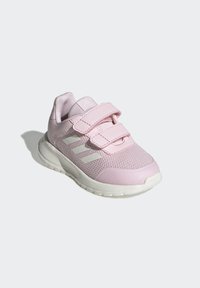 Zapatilla deportiva rosa con parte superior de malla, dos correas de velcro y suela de goma blanca con tres rayas blancas en el costado.