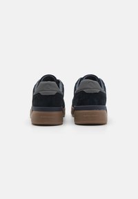 Sneakers em camurça azul-marinho com detalhes cinza, forma arredondada na parte de trás, colarinho acolchoado e solas de borracha com o nome da marca estampado no calcanhar.