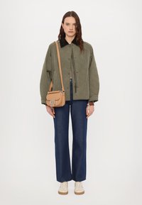 Gepolsterte olivgrüne Jacke mit schwarzem Kragen, kombiniert mit blauen weiten Jeans und beigen Sneakers. Zudem verfügt sie über eine kleine tanfarbene Umhängetasche.