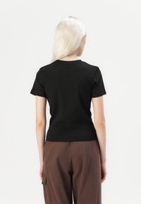 Juoda trumpa rankovė t-shirt su apvalia kaklo iškirpte, prigludusios formos ir lygiu medvilnės audiniu. Dėvimi su rudos spalvos laisvai krentančiomis kelnėmis.