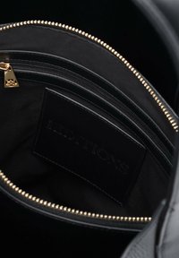 Interno di una borsa a tracolla nera in pelle con una tasca con zip, hardware color oro e un'etichetta cucita. Texture liscia con fodera in tessuto nero.