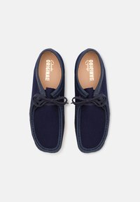 Par de sapatos estilo mocassim, de cor azul-marinho, com acabamento em pele e atacadores, vistos de cima sobre um fundo branco.