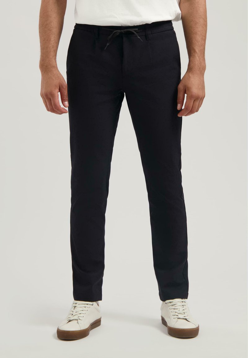 Pantalons noirs cintrés en tissu léger, avec une taille élastique à cordon. Assortis à des baskets blanches pour un look décontracté.