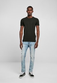 Camiseta negra de manga corta combinada con jeans de mezcla clara y zapatillas negras con cordones blancos. Ajuste casual y diseño sencillo.