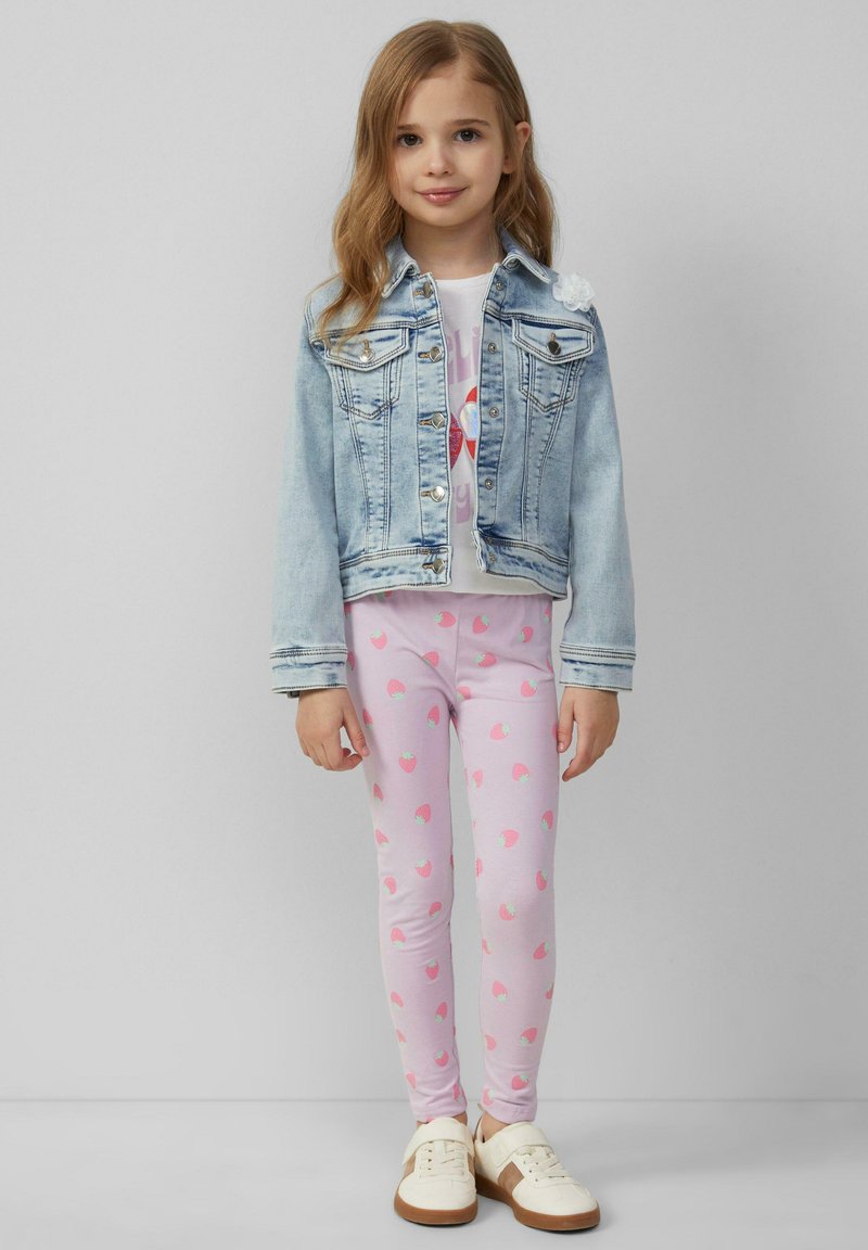 Denim jack met lichtblauwe tint en zilverkleurige hardware, wit T-shirt met grafische print, roze leggings met aardbeienpatroon, crème sneakers.