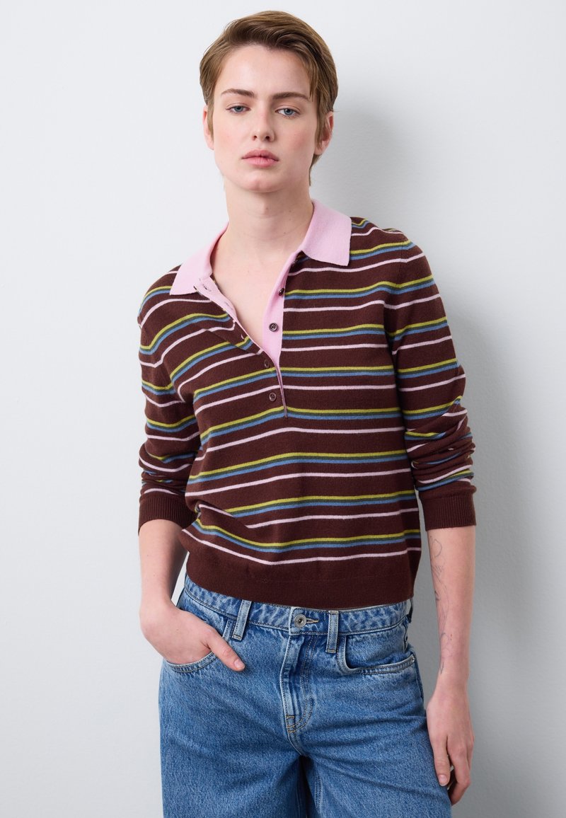 Suéter marrón a rayas con un cuello rosa claro, con rayas horizontales en azul y verde. Combinado con jeans de tiro alto en azul claro.