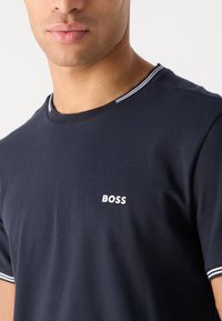 Tumši zils t-krekls no kokvilnas ar apaļu kakla izgriezumu, balta "BOSS" emblēma uz krūtīm un kontrastējoša svītru apdare uz apkakles.