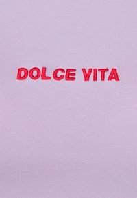 Texte brodé rouge « DOLCE VITA » centré sur un fond en tissu côtelé violet clair.