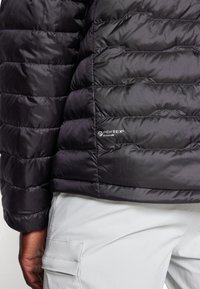 Black insulated jacket with quilted design, featuring PERTEX Quantum logo. Smooth texture and lightweight material ideal for warmth and comfort.