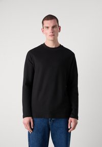 Sudadera negra de manga larga y cuello redondo, hecha de un material suave, con una textura lisa y un corte relajado, combinada con jeans de mezclilla azul.