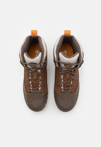 Hnědé turistické boty s texturovanou, tečkovanou gumovou podrážkou. Mají šedé akcenty, polstrovaný límec a oranžový poutko pro snadné obouvání.
