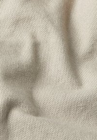 Tessuto beige con texture e un motivo intrecciato, che mostra una superficie morbida e leggermente elastica, con pieghe e grinze sottili.