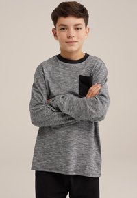 Siva majica z dolgimi rokavi iz teksturirane, melange tkanine, s kontrastnim črnine krožnim ovratnikom in majhnim črnim žepom na levi prsni strani.