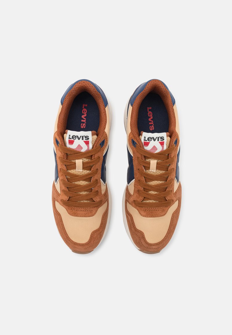 Brune og marineblå sneakers med en overdel i ruskind og tekstil, der har snørebånd, en polstret krave og en logoetiket på tungen.